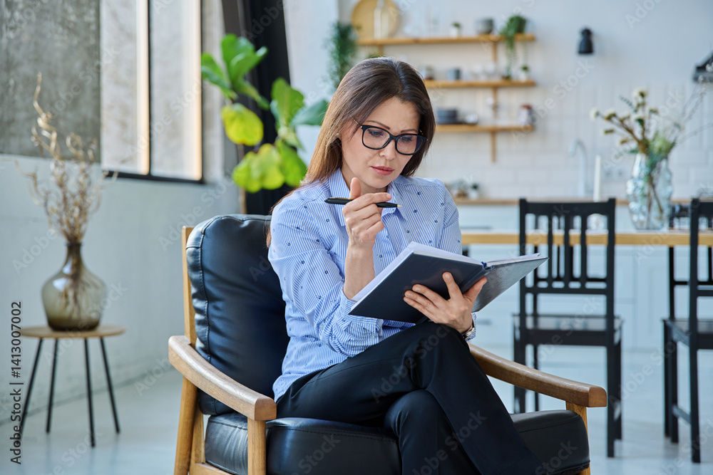 Mature confident businesswoman with notepad sitting in chair