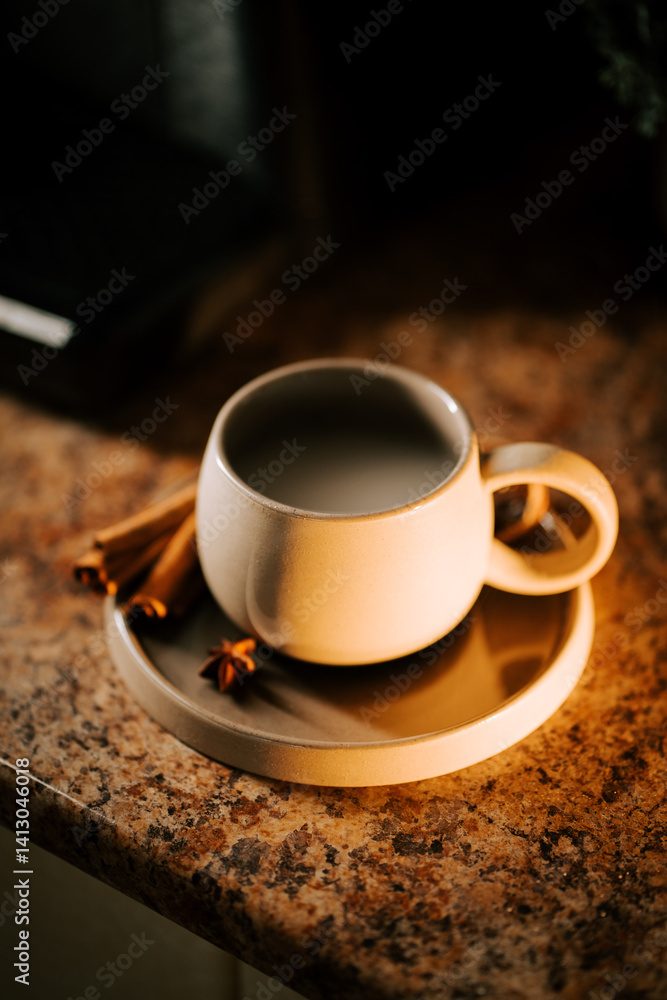 Fototapeta premium Warm cup of coffee on a cozy countertop with cinnamon sticks nearby during morning light