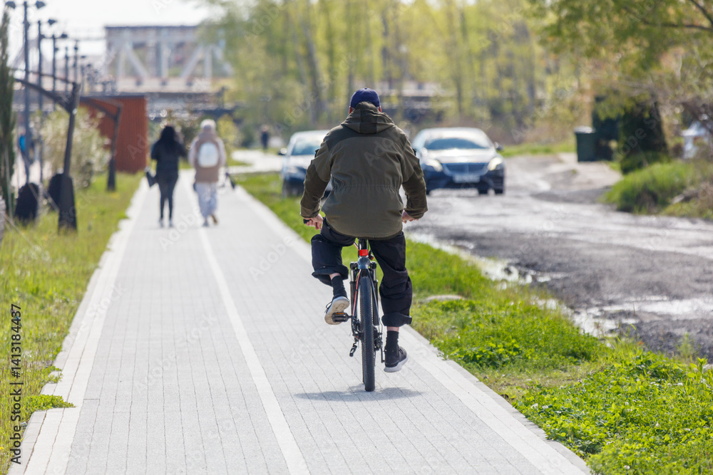 A man rides a bike down a sidewalk next to a road A man rides a bike down a sidewalk next to a road