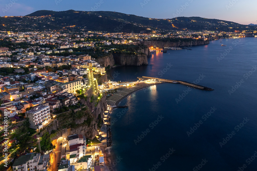 Fototapeta premium Blue hour view of the Sorrento Coast, Italy, with the city lights glowing against the twilight sky. The coastline, perched above the Mediterranean Sea