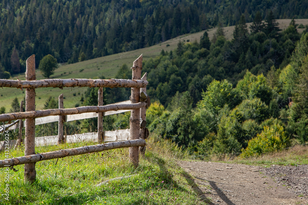Rustic wooden fence along a peaceful hillside trail surrounded by lush greenery under a clear sky