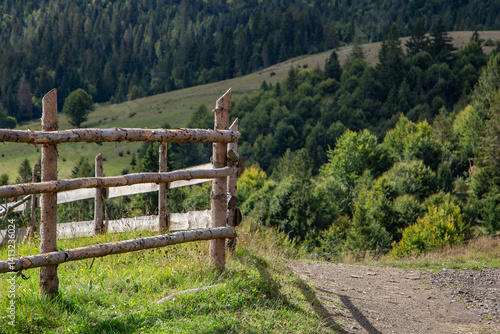 Obraz na płótnie Rustic wooden fence along a peaceful hillside trail surrounded by lush greenery under a clear sky w salonie