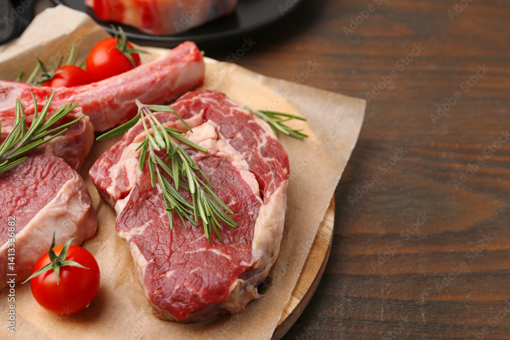 Pieces of raw beef, rosemary and tomatoes on wooden table, closeup. Space for text Pieces of raw beef, rosemary and tomatoes on wooden table, closeup. Space for text