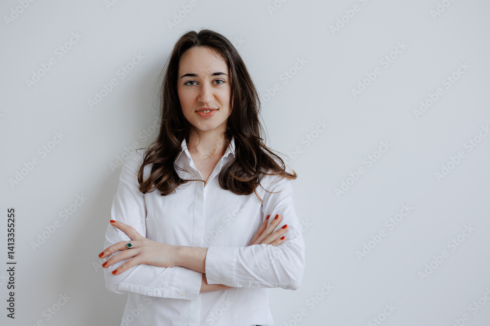 Confident woman posing in a white button-up shirt against a light wall background in a minimalist setting Confident woman posing in a white button-up shirt against a light wall background in a minimalist setting