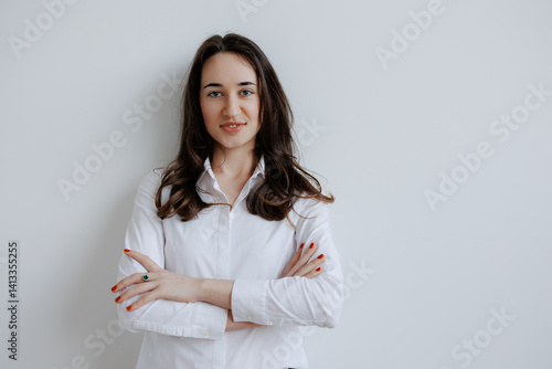 Confident woman posing in a white button-up shirt against a light wall background in a minimalist setting