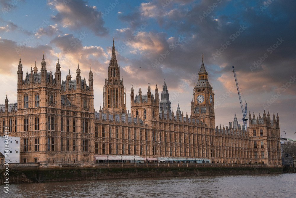 The Palace of Westminster and Big Ben in London, England, with Gothic Revival architecture, a dramatic sky, and the River Thames in the foreground.