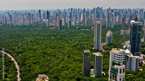 Aerial view of a modern city with tall skyscrapers, roads filled with traffic, and green parks scattered across the urban landscape.