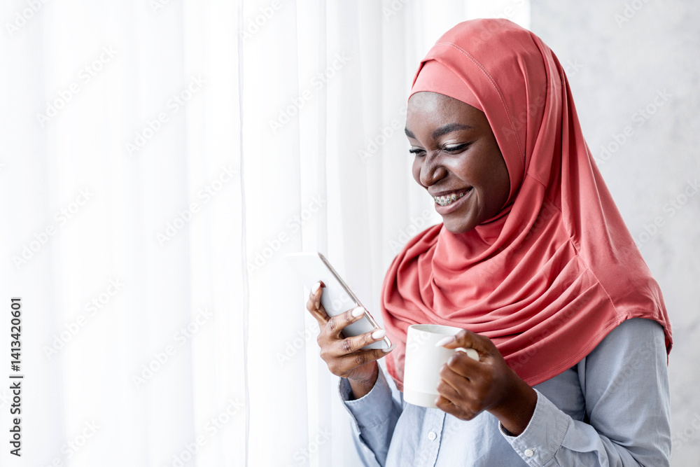 Relaxing Morning. Smiling Black Muslim Woman In Hijab Drinking Coffee And Using Smartphone At Home, Standing Near Window, Enjoying Hot Drink And Mobile Communication, Reading Messages, Copy Space Relaxing Morning. Smiling Black Muslim Woman In Hijab Drinking Coffee And Using Smartphone At Home, Standing Near Window, Enjoying Hot Drink And Mobile Communication, Reading Messages, Copy Space