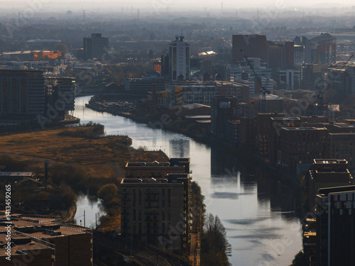 Aerial perspective of Manchester, UK, showing a river winding through skyscrapers, modern buildings, construction cranes, and patches of greenery.