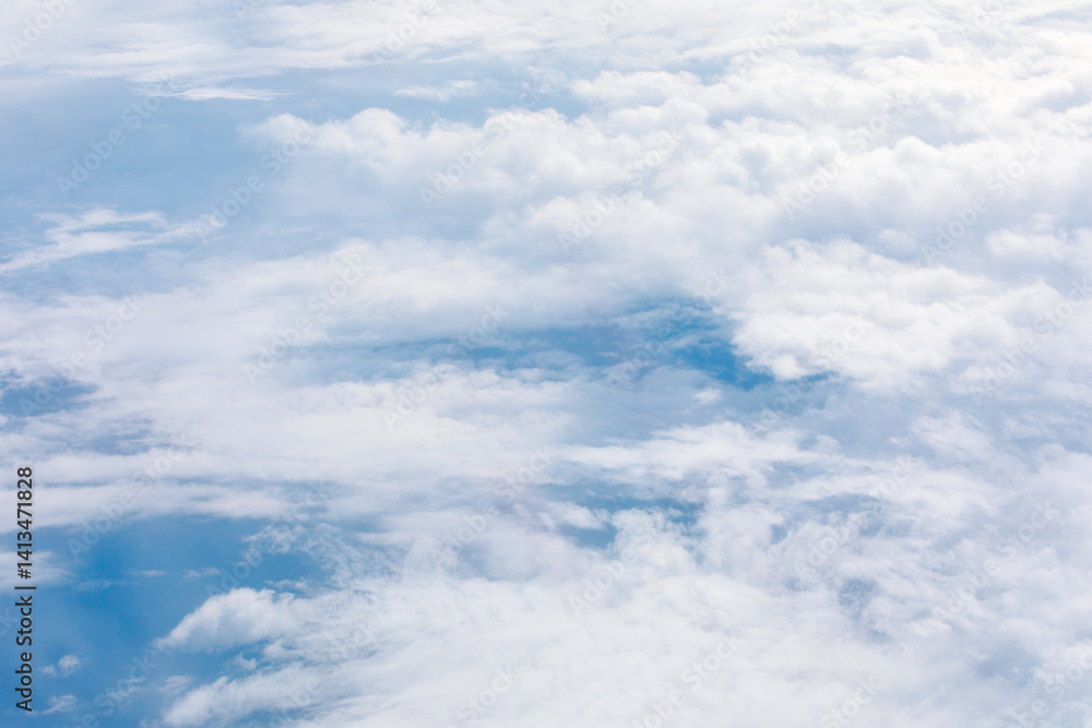 An aerial view reveals a vast expanse of fluffy white clouds floating over a serene blue sky. Ethereal scene, with hints of the earth below, is perfect for atmospheric theme