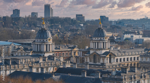 The domed buildings of the Old Royal Naval College in Greenwich, London, stand out with classical architecture, set against a modern urban skyline.