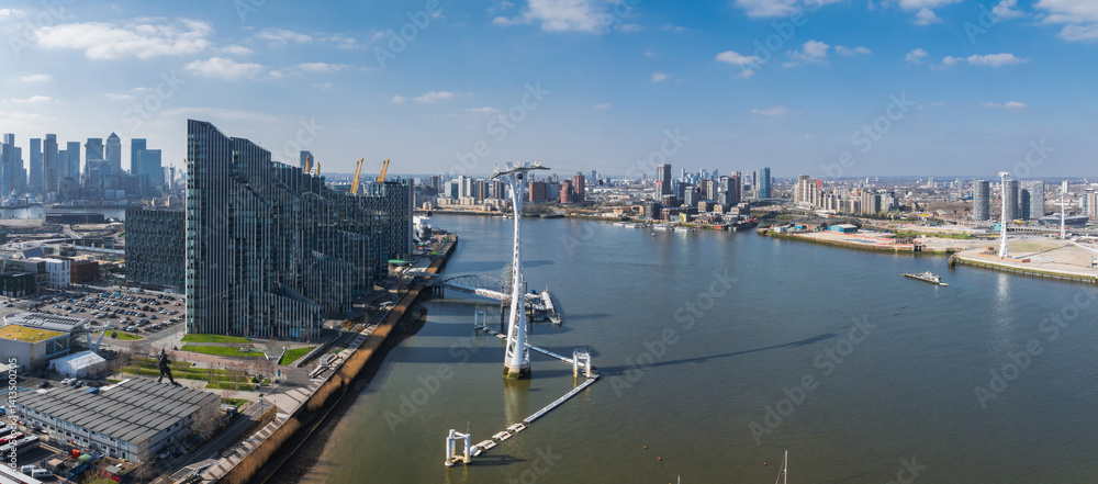 Aerial perspective of London featuring the River Thames, Canary Wharf skyscrapers, Emirates Air Line cable cars, and urban architecture under clear skies.