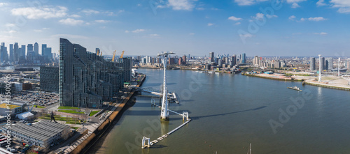 Aerial perspective of London featuring the River Thames, Canary Wharf skyscrapers, Emirates Air Line cable cars, and urban architecture under clear skies.