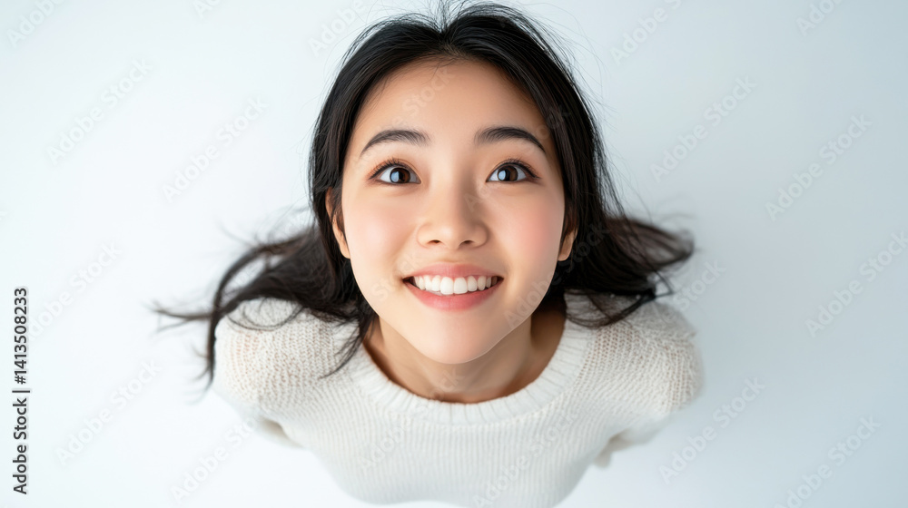 Cheerful young asian woman smiling upwards in white sweater with bright eyes and long dark hair on a soft white background