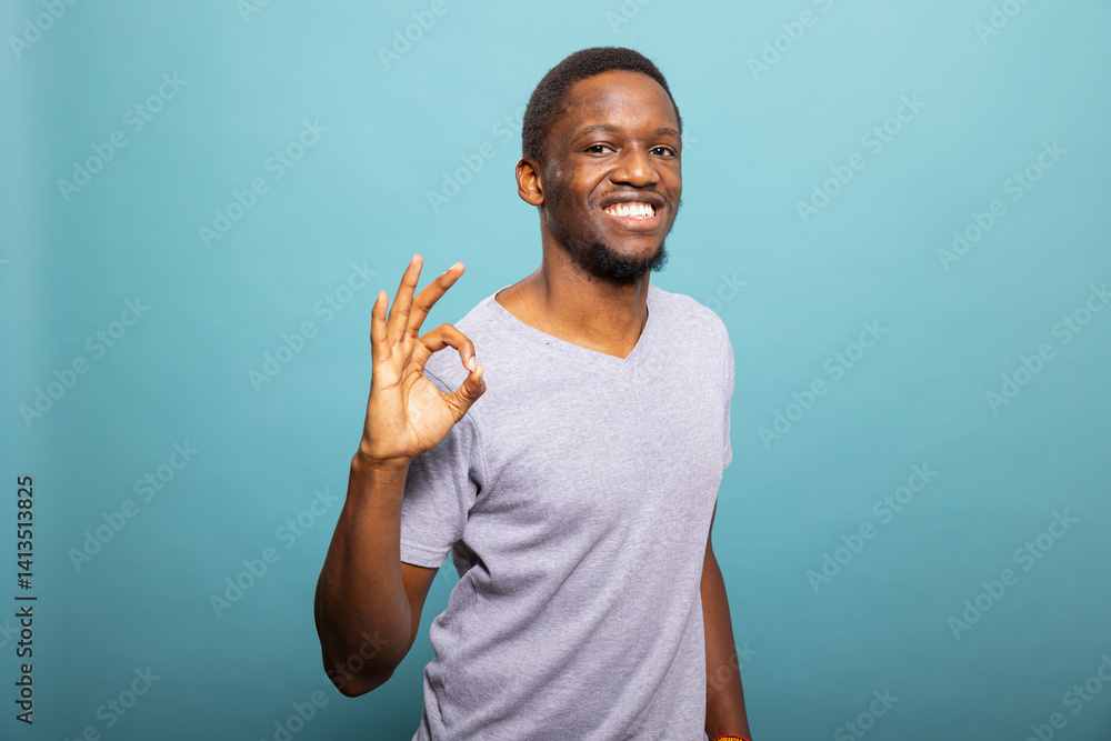 Black male individual smiling at the camera while making an approval gesture with his fingers. Smiling african american man making an okay hand sign, expressing agreement and satisfaction.