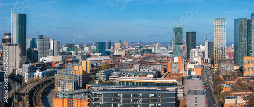 Obraz na płótnie Aerial view of Manchester, UK, showcasing skyscrapers, construction cranes, a railway line, and a mix of modern and historic architecture under a clear sky. w salonie