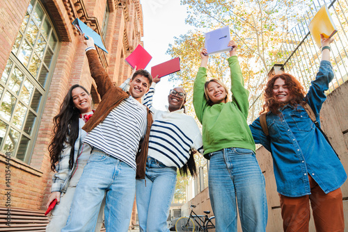 Canvas-taulu Group of enthusiastic students cheerfully lifting their notebooks in a triumphant academic success, embodying the spirit of teamwork and friendship during their time at school and university