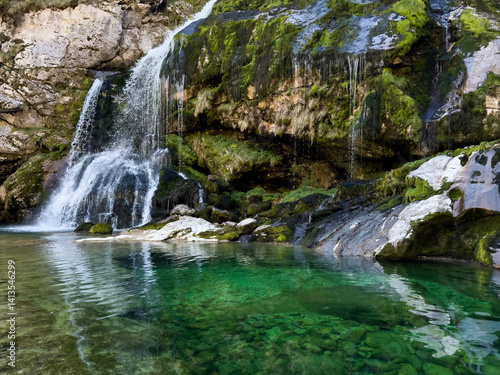 scenic mountain waterfall cascading over mossy rocks into a crystal clear emerald natural mountain pool. natural tranquil scene rich in