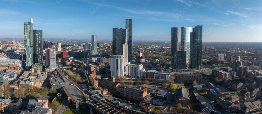 Aerial view of Manchester, UK, on a sunny day featuring Beetham Tower, Deansgate Square, historic and modern architecture, roads, canals, and greenery.