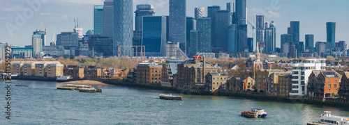 Obraz na płótnie A vibrant aerial view of London's Canary Wharf skyline with modern skyscrapers, the River Thames, historic brick buildings, and boats on the water. w salonie