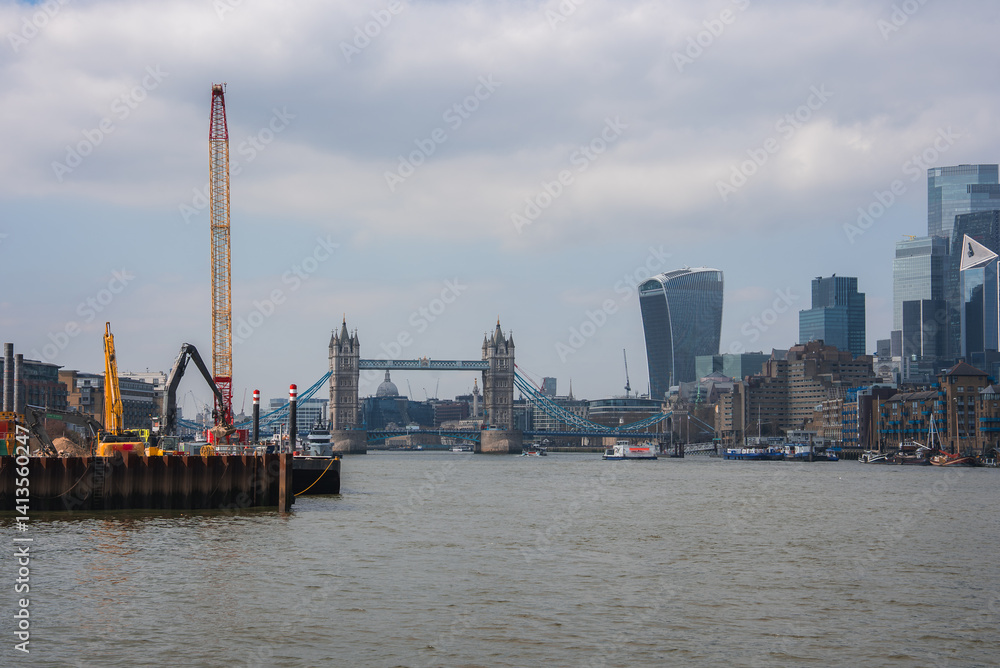 View of Tower Bridge over the River Thames in London, with modern skyscrapers like the Walkie Talkie building and construction cranes on the riverbank.