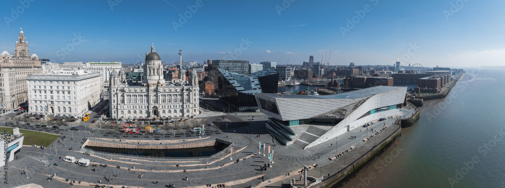 Aerial image of Liverpool's waterfront showing the Royal Liver Building, Port of Liverpool Building, Museum of Liverpool, and bustling promenade by the River Mersey.