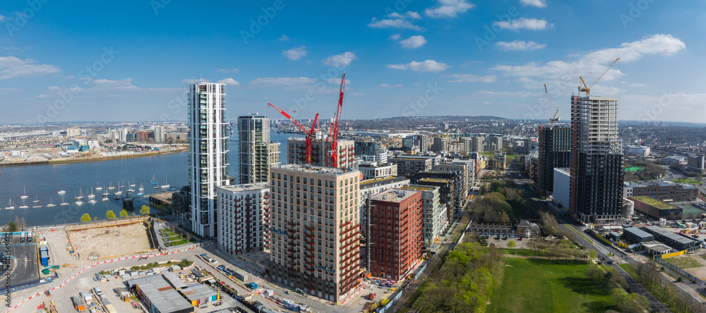Aerial view of London's urban area with high rise buildings, construction cranes, the River Thames on the left, and a green park in the foreground.