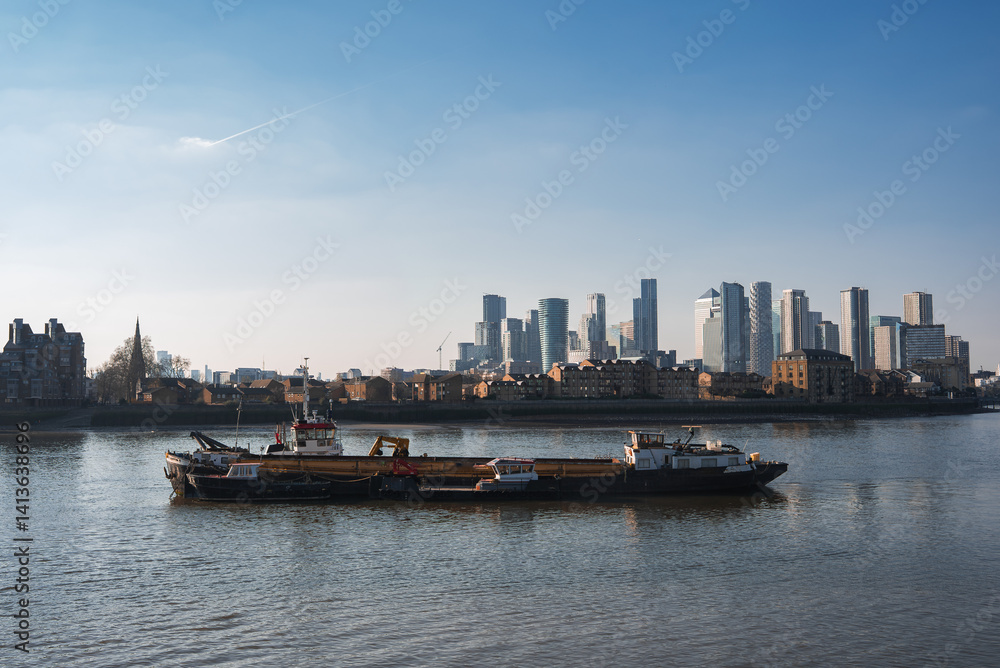 The River Thames features a barge and boats in the foreground, with Canary Wharf's skyscrapers and a church spire contrasting historic and modern London.
