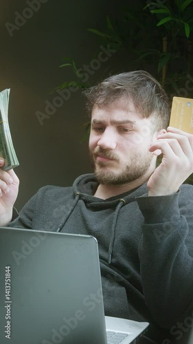 Confused young man comparing cash and credit card while shopping online at home ,vertical video