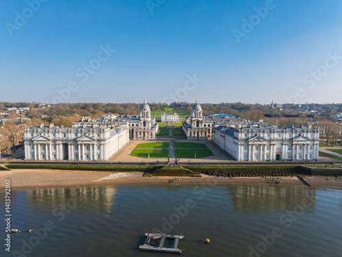 Aerial view of the Old Royal Naval College in Greenwich, London, featuring twin domed buildings, the Queen's House, and the River Thames in the foreground.