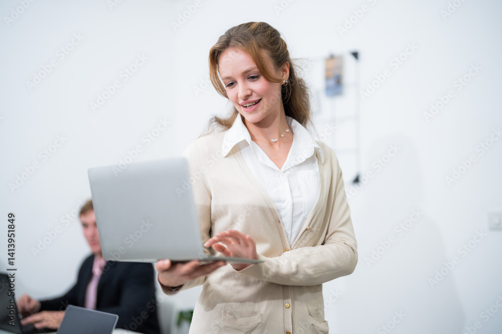 Woman using laptop while smiling in a modern office setup with coworkers focused on their work Woman using laptop while smiling in a modern office setup with coworkers focused on their work