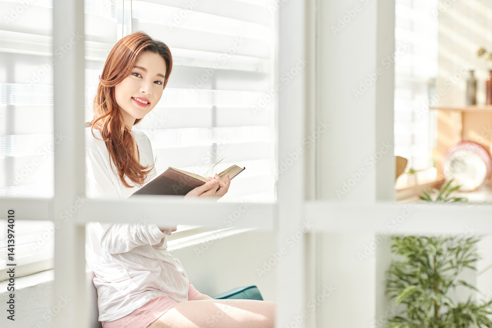 Young Woman Reading Book Indoors by Window Young Woman Reading Book Indoors by Window
