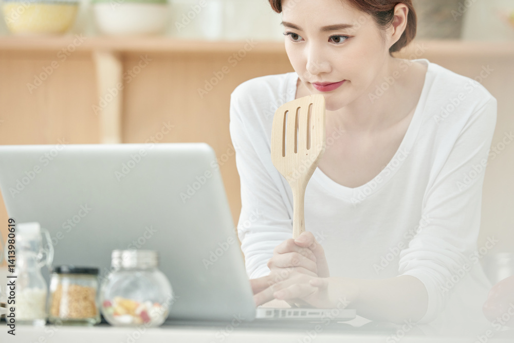 Young Woman in Kitchen Using Laptop for Cooking