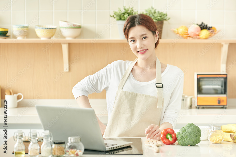Smiling Woman in Apron Cooking with Laptop in Modern Kitchen Smiling Woman in Apron Cooking with Laptop in Modern Kitchen