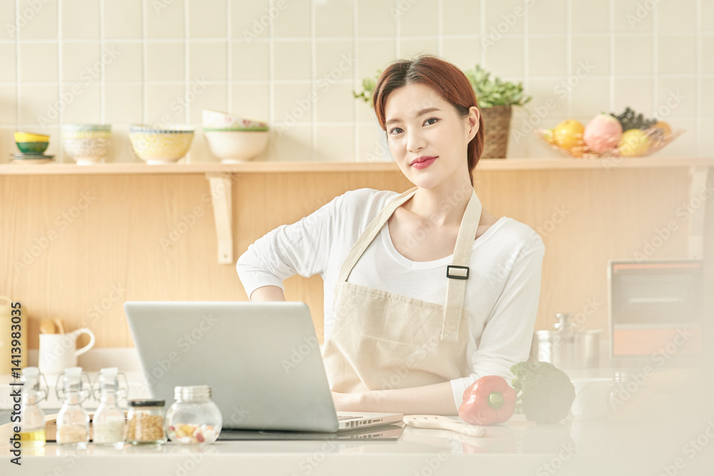 Smiling Woman in Apron Cooking with Laptop in Modern Kitchen Smiling Woman in Apron Cooking with Laptop in Modern Kitchen