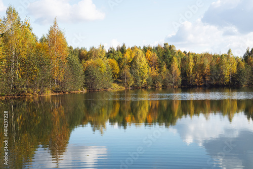 Autumn landscape with a lake and trees in the background. Golden autumn sunny day. Water surface with forest reflection in water. Parks and country recreation. Walks in the forest by the pond