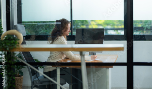 Young woman focused on work in modern office space with large windows allowing natural light