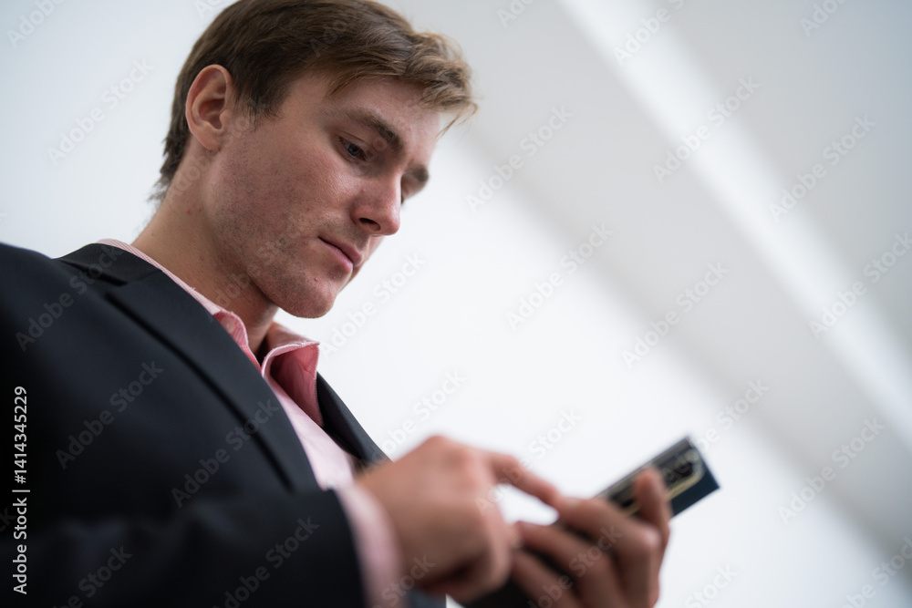 Young man checking messages on smartphone while dressed in a modern suit in an indoor setting during the day Young man checking messages on smartphone while dressed in a modern suit in an indoor setting during the day