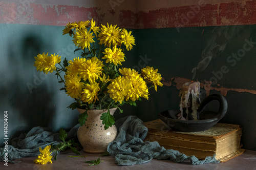 A bouquet of yellow chrysanthemums and an extinguished candle, on a dark background.