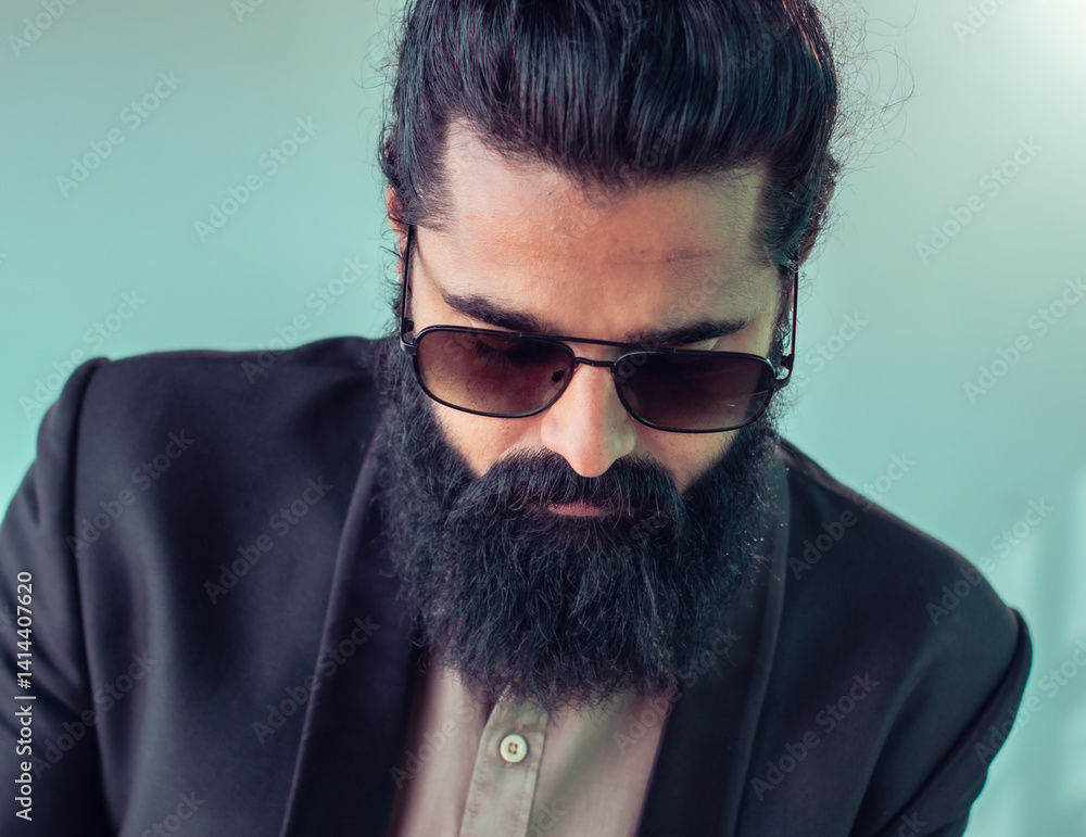 Obraz premium Portrait of a fashionable man with a thick beard and sunglasses, dressed in a formal suit, exuding confidence and style while wearing a contemporary expression against a relaxed, modern background.
