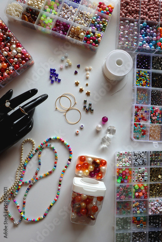 Hand figurine, colorful friendship bracelets, necklaces, various beads and DIY supplies on the table. Making jewelry at home. Flat lay.