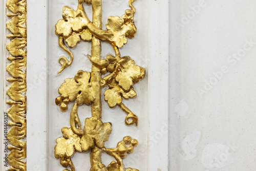 Detailed view of intricate gold leaf decorations on a white ornamental wall