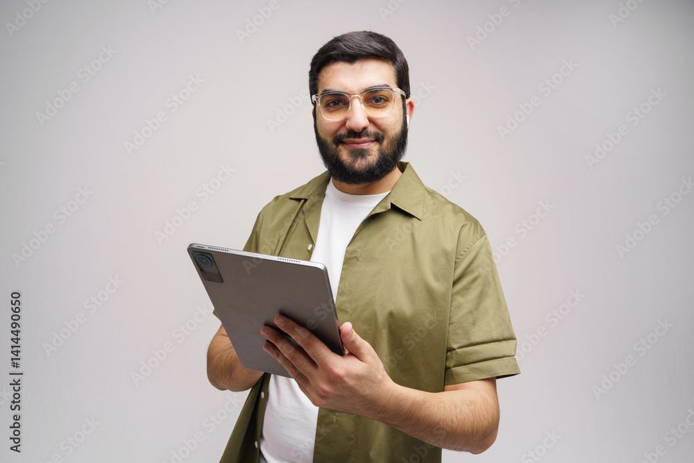 Smiling Man in Casual Attire Holding a Tablet While Standing Against a Minimalistic Background Indoors Smiling Man in Casual Attire Holding a Tablet While Standing Against a Minimalistic Background Indoors