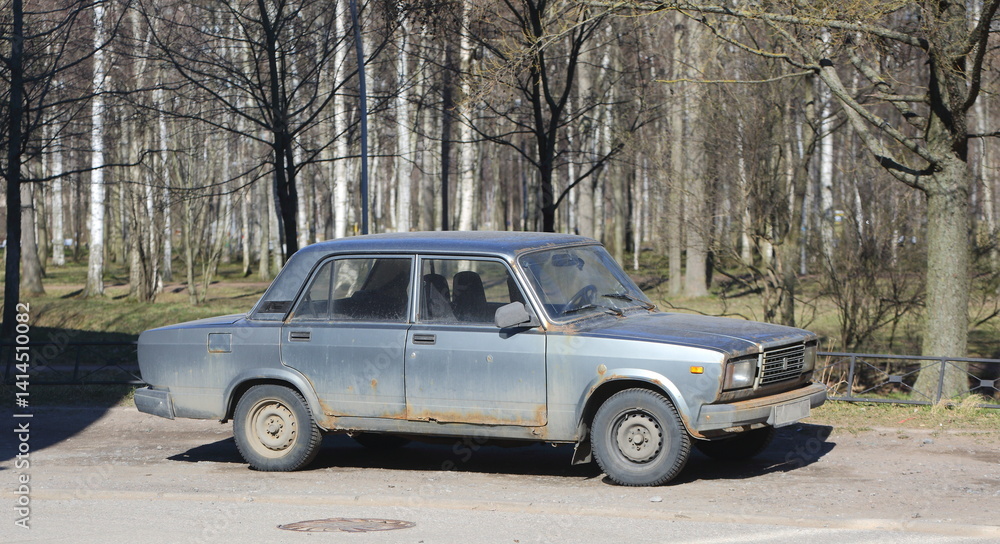 Bolshevikov Avenue, St. Petersburg, Russia, April 15, 2025: An old gray rusty Soviet car is parked near the outskirts of the park Bolshevikov Avenue, St. Petersburg, Russia, April 15, 2025: An old gray rusty Soviet car is parked near the outskirts of the park