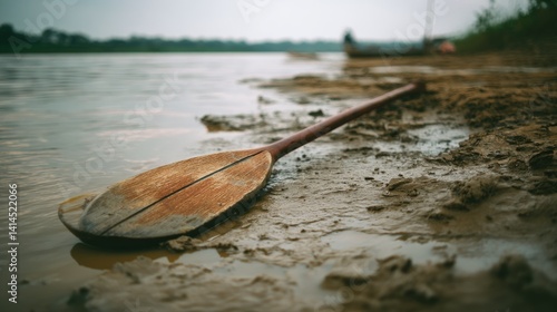 Obraz na płótnie A solitary oar lies on muddy riverbank, reflecting tales of tranquil wanderings under a muted sky. w salonie
