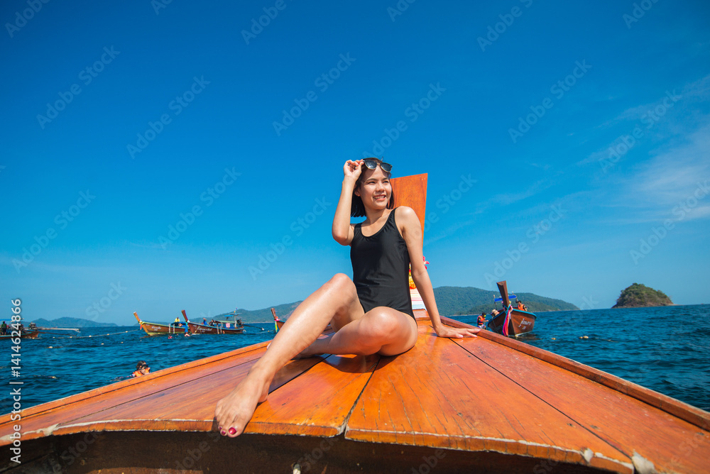 Obraz na plátně Asian woman wearing a one-piece swimming suit sitting on the ship prow of wooden Traditional Thai long-tail Tourist boat on wide sea or ocean