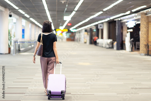 Back of view Motion A lonely woman wearing casual tourist drag and carry luggage in the Airport terminal. One person in the walkway in the terminal of the passenger. Travel and Holiday concept.