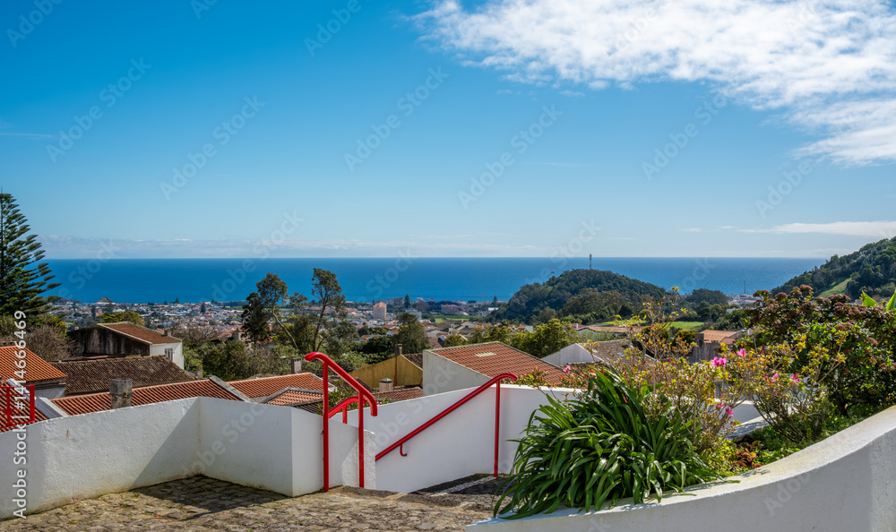 Fototapeta premium Moinho de Vento da Tia Faleira, Fajã de Cima, São Miguel, Azoren: Panoramablick über Ponta Delgada und Pico da Barrosa. Blauer Himmel, Sonne und grüne Landschaft prägen die Szenerie.