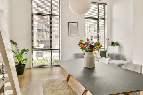 A stylish modern living space featuring natural light, a minimalist table, potted plants, and decorative flowers in a vase, highlighting comfort and elegance.
