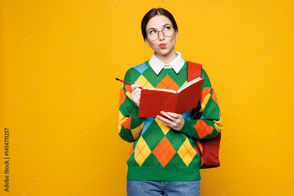 Young minded pensive girl student wears green casual clothes backpack bag hold book write down in notebook isolated on plain yellow background studio portrait. High school university college concept. Young minded pensive girl student wears green casual clothes backpack bag hold book write down in notebook isolated on plain yellow background studio portrait. High school university college concept.